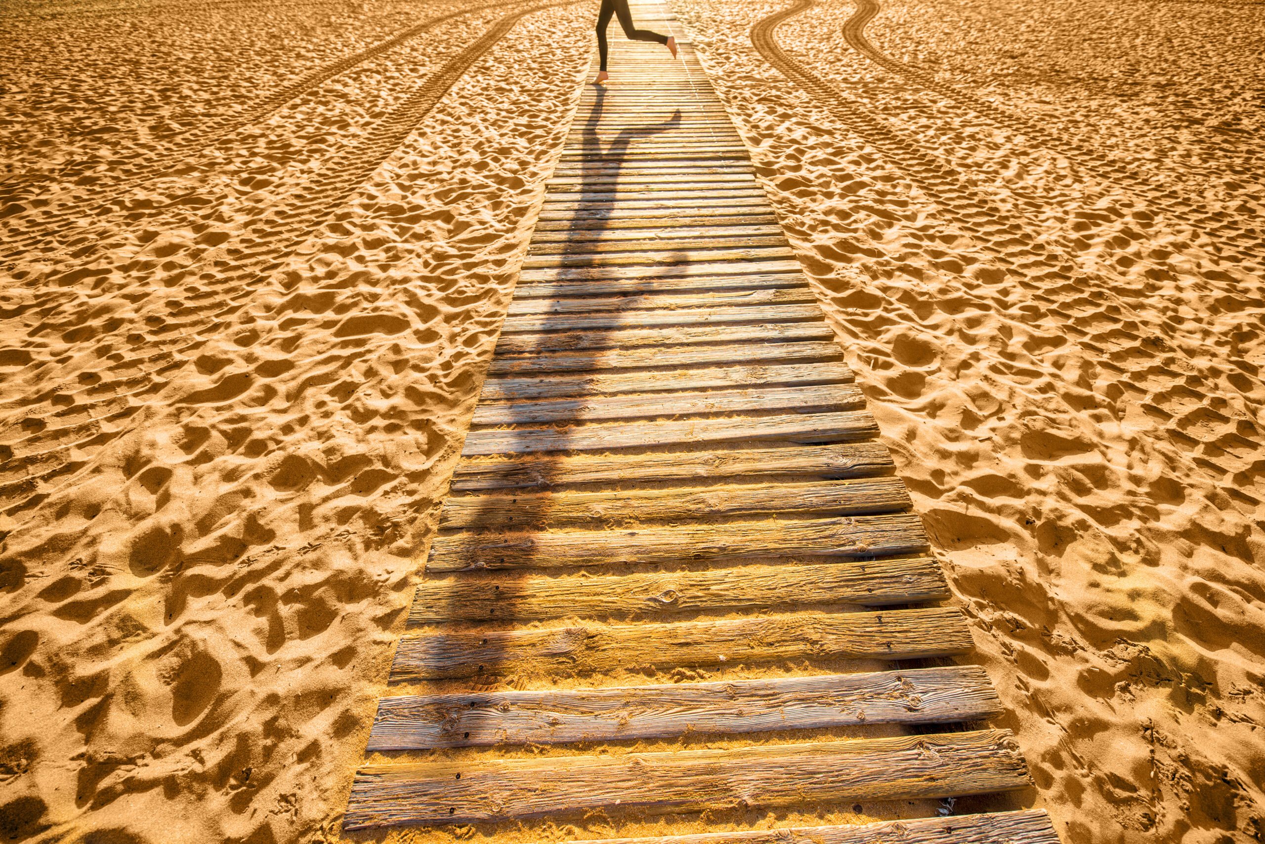 View on sandy beach with wooden footpath and shadow of running woman